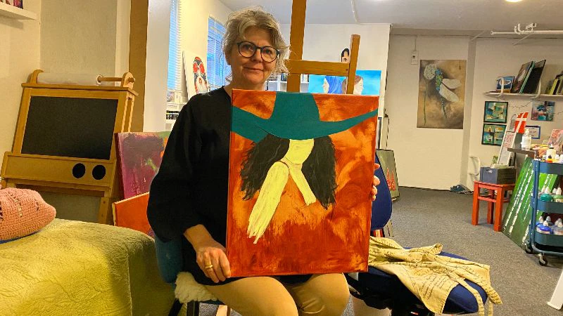 Helle sidder på en stol og viser sit maleri frem