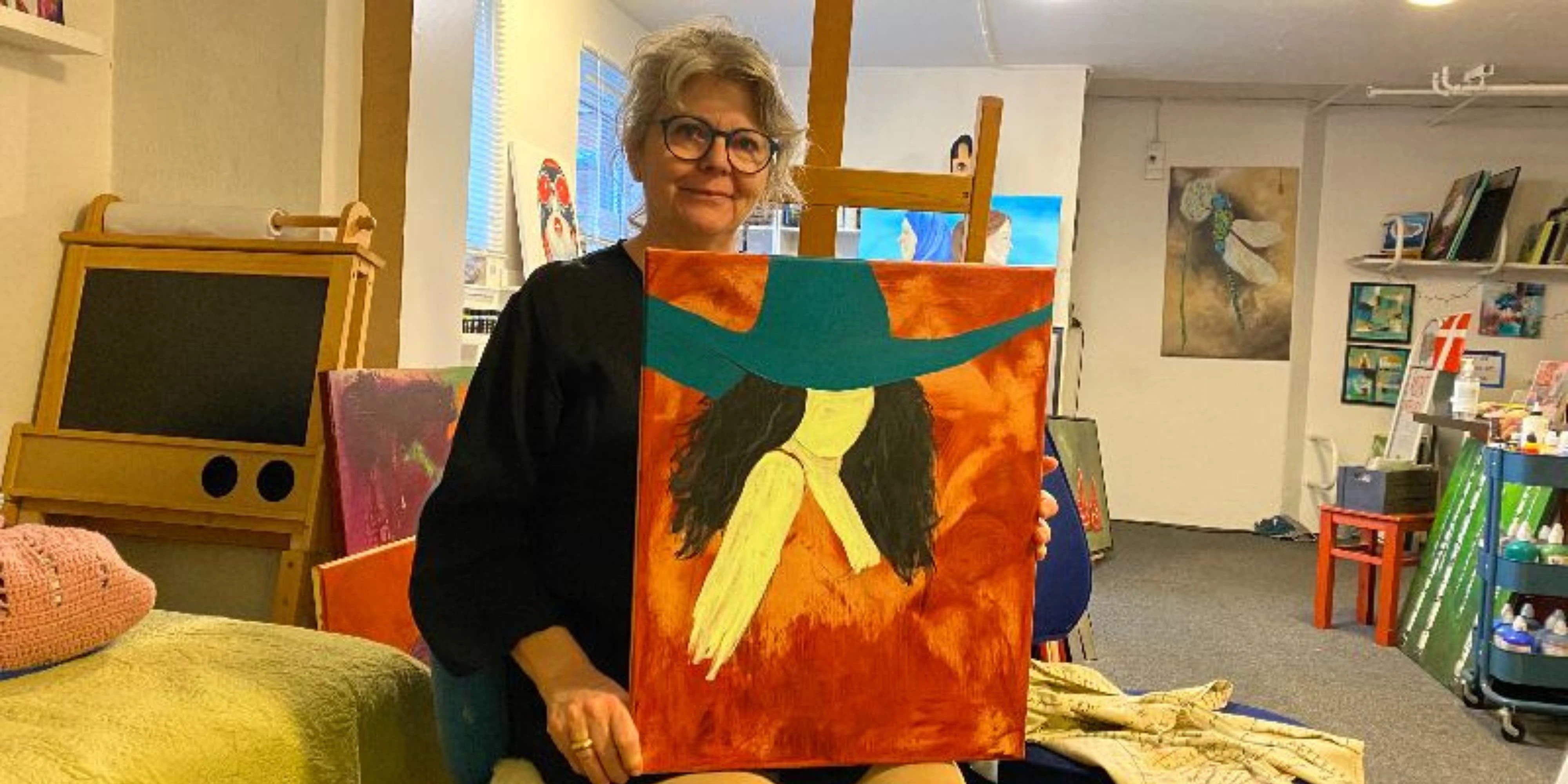 Helle sidder på en stol og viser sit maleri frem